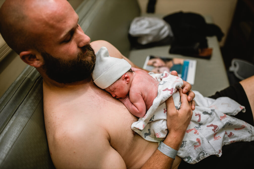 Father holding his newborn baby skin-to-skin on his chest during early bonding in the hospital.