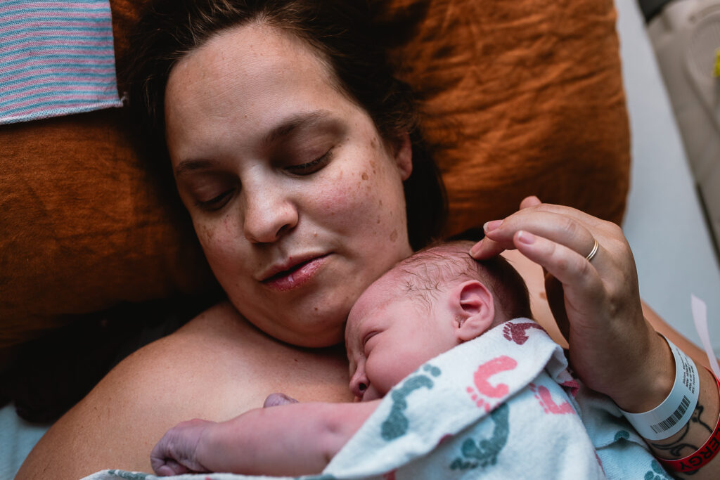 Mother resting in bed while holding her newborn close after birth.