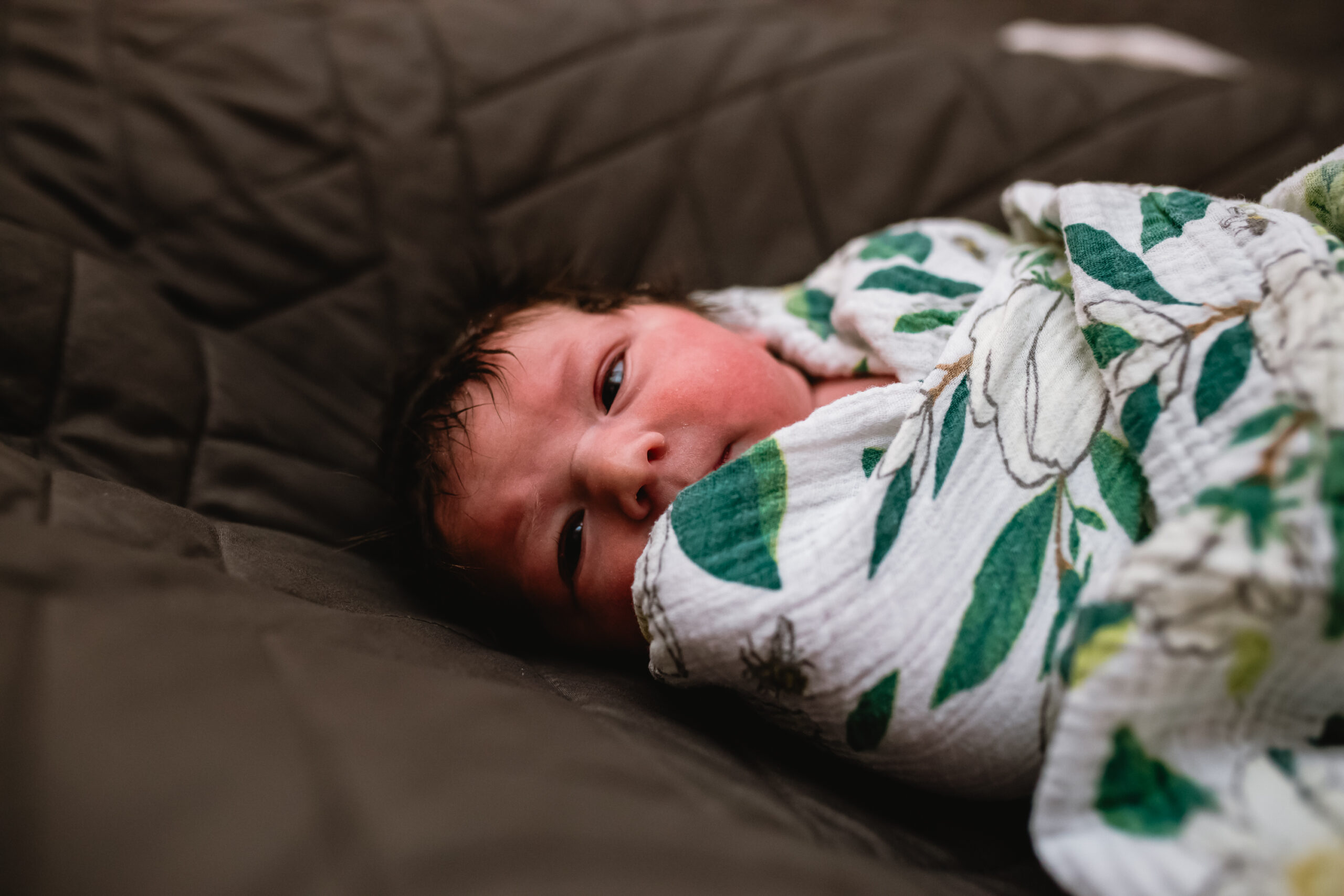 Newborn baby swaddled in a floral blanket looking toward the camera during a Fort Worth birth photography session.