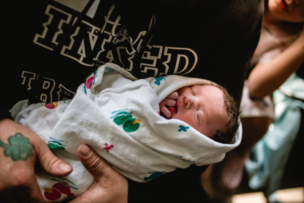 Newborn baby wrapped in a hospital blanket resting peacefully in a parent’s arms during a Fort Worth birth photography session.