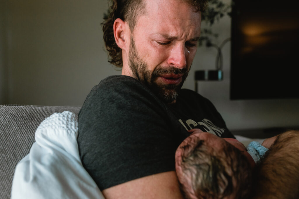 Emotional father holding his newborn baby for the first time during an in-home birth session in Fort Worth