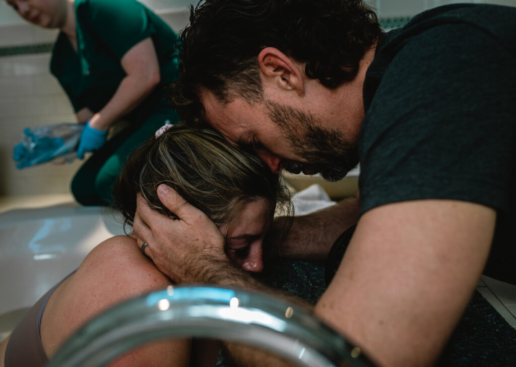 Father holding his partner’s hand during labor in Fort Worth, allowing him to stay fully present while a birth photographer documents the moment.
