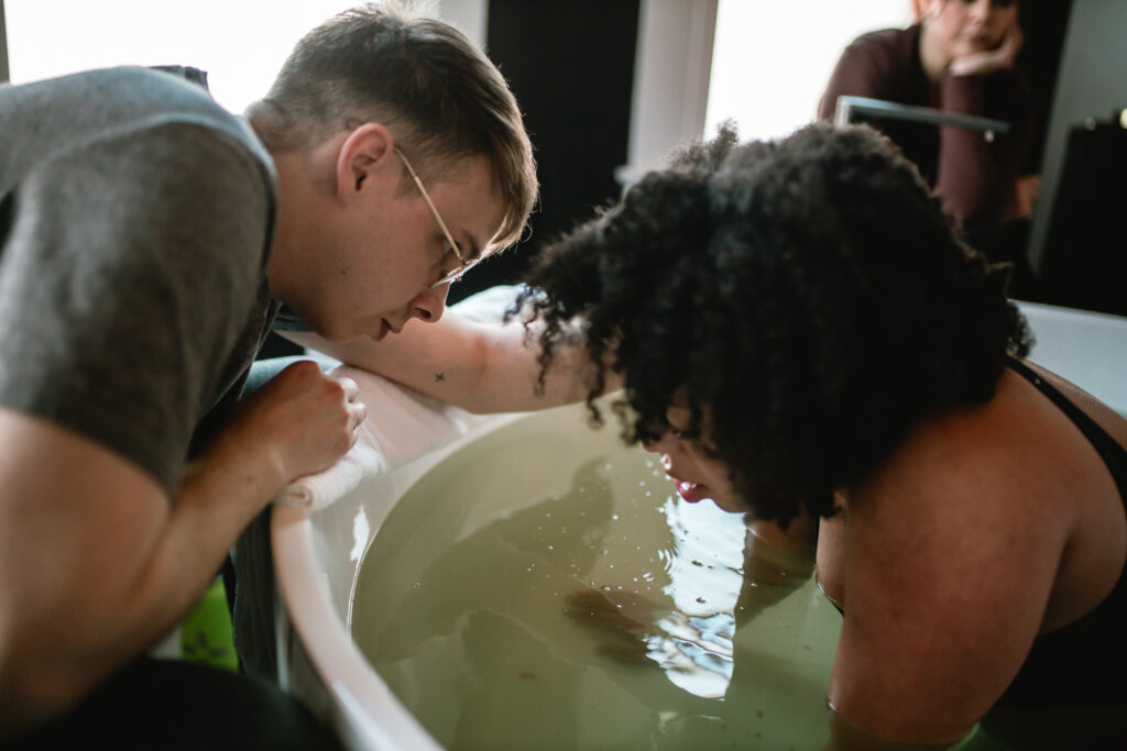 Husband leans into the birth tub, offering steady support as his wife labors in warm water at the birth center