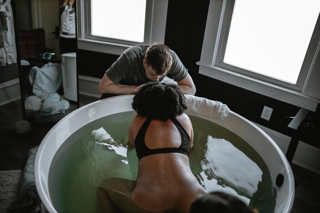 Midwife gently supporting the laboring mother’s arms as she works through a surge in the birth tub