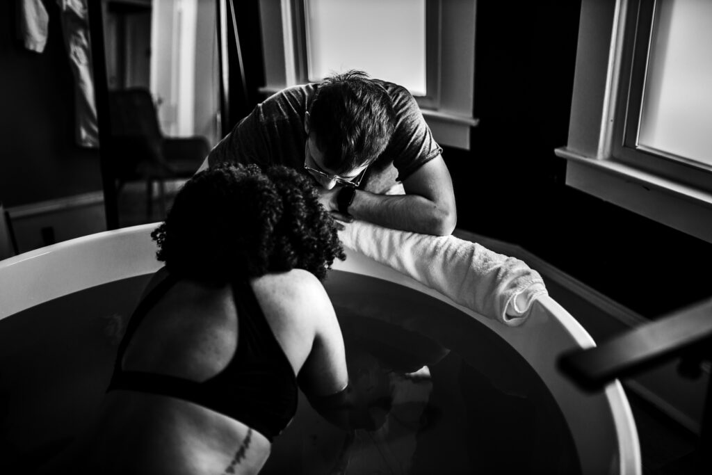 Birth partner holding the mother close while she labors in the warm water under soft window light
