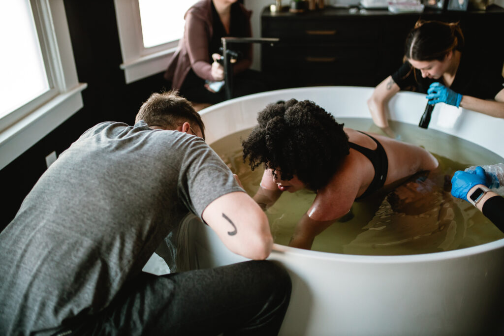 Birth team gathered calmly around the mother as she labors in the birth tub