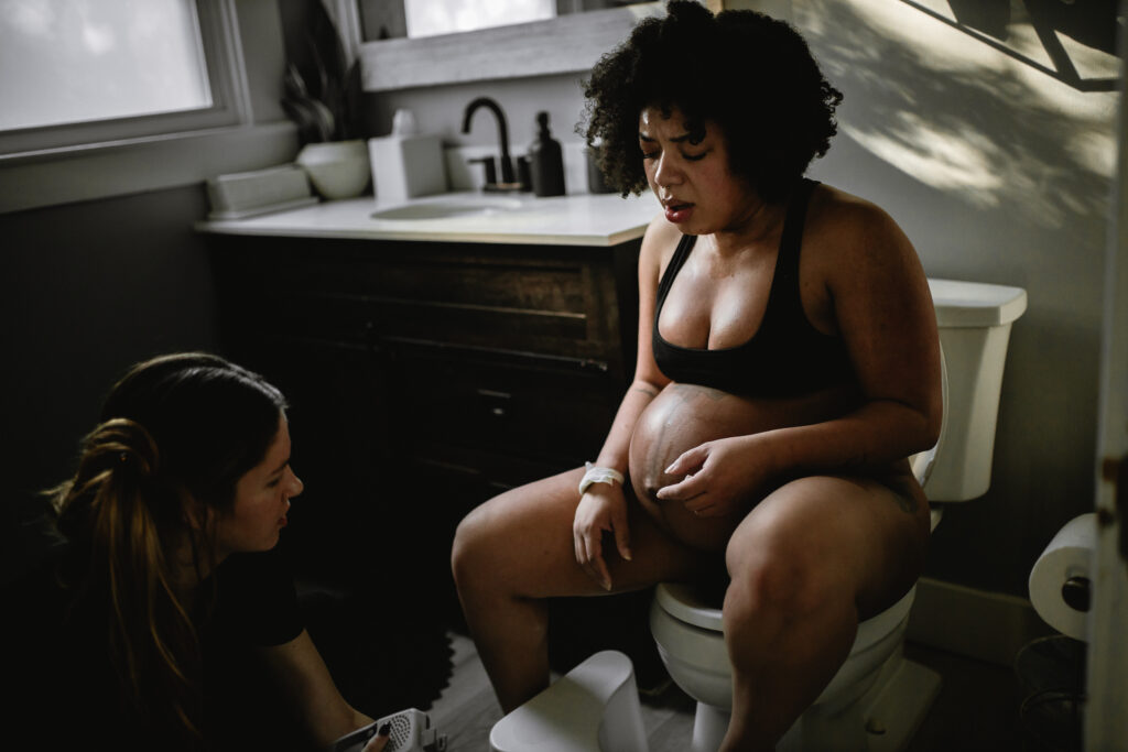 Mother seated in the bathroom near the birth center vanity, breathing and resting during labor