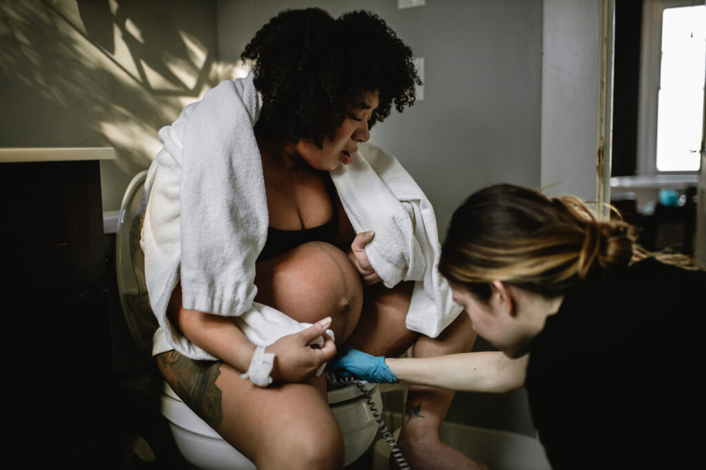 Mother laboring on the birth stool with a towel over her shoulders while the midwife gently supports her