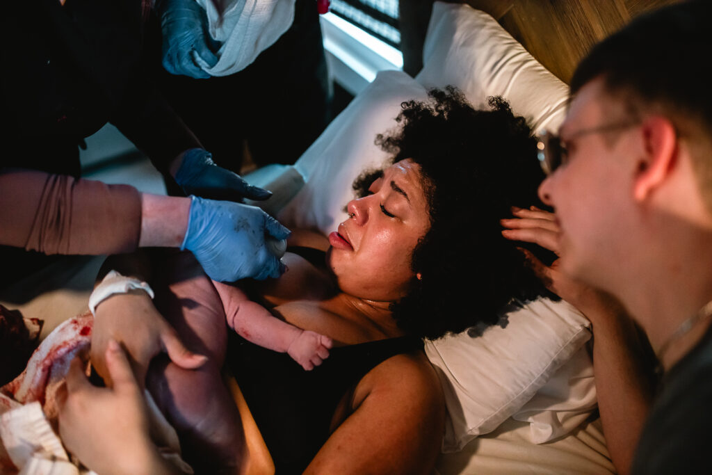 Midwife gently guiding the baby into the mother’s arms as she delivers on the bed