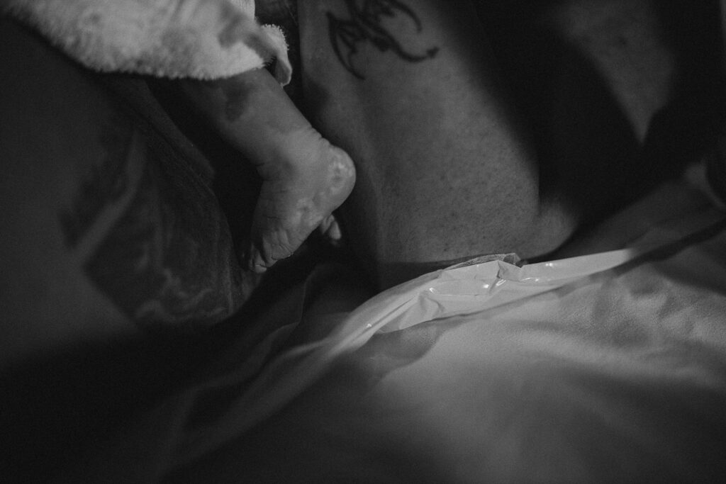 Close-up of the newborn’s tiny feet and wrinkled toes resting against the sheets after birth