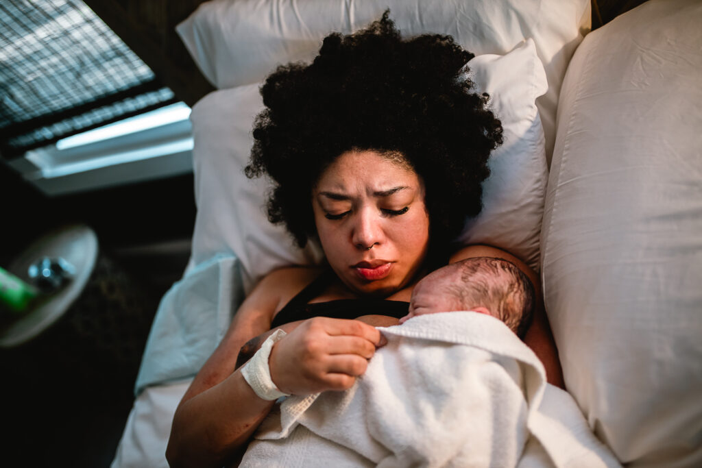 Mother lying in bed with her newborn resting on her chest, wrapped in a white blanket, eyes closed in peaceful recovery