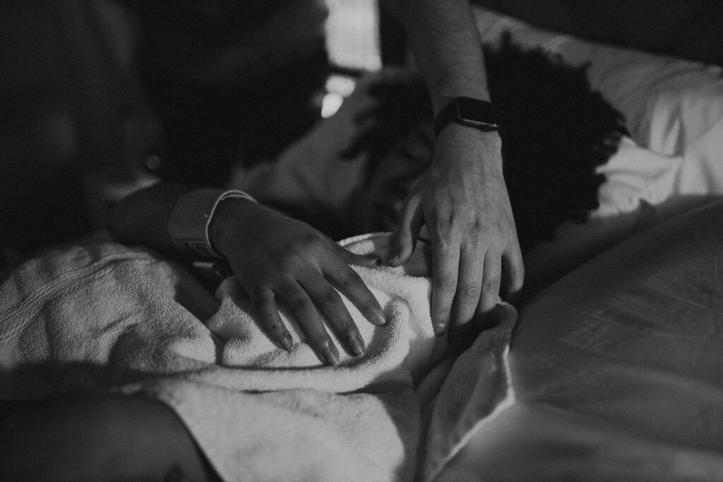 Black and white photo of the mother’s hand gently cradling her newborn’s tiny body after birth