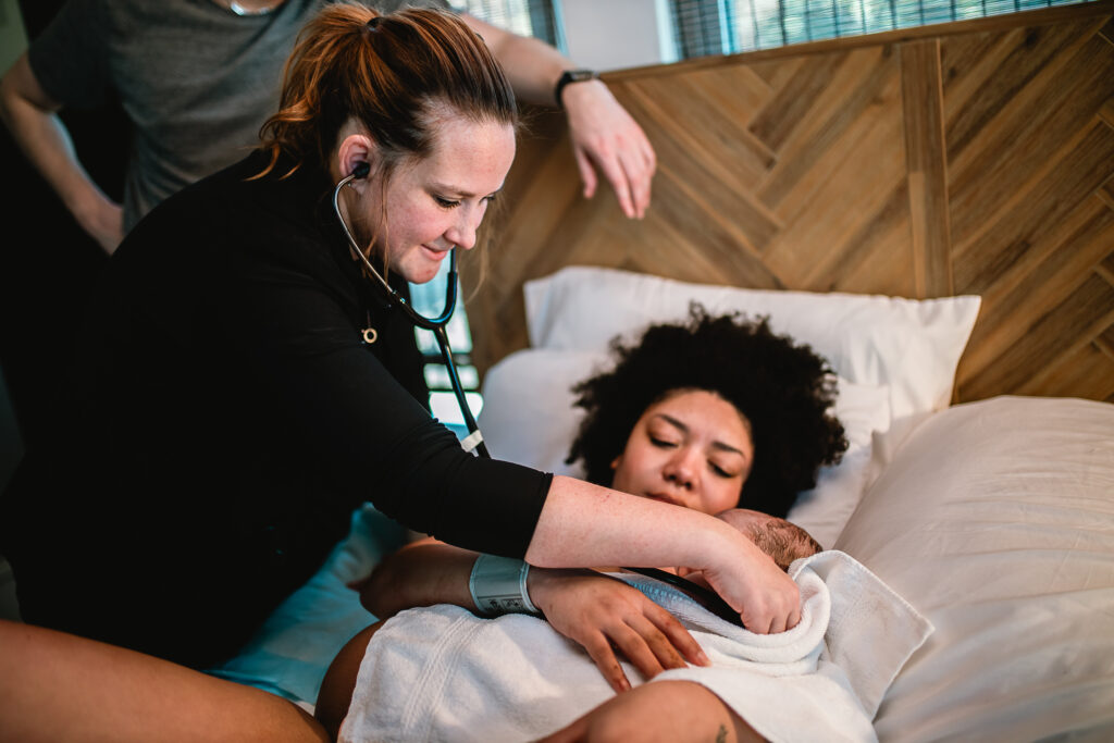 Midwife listening to the baby’s heartbeat while the mother holds her newborn close on her chest