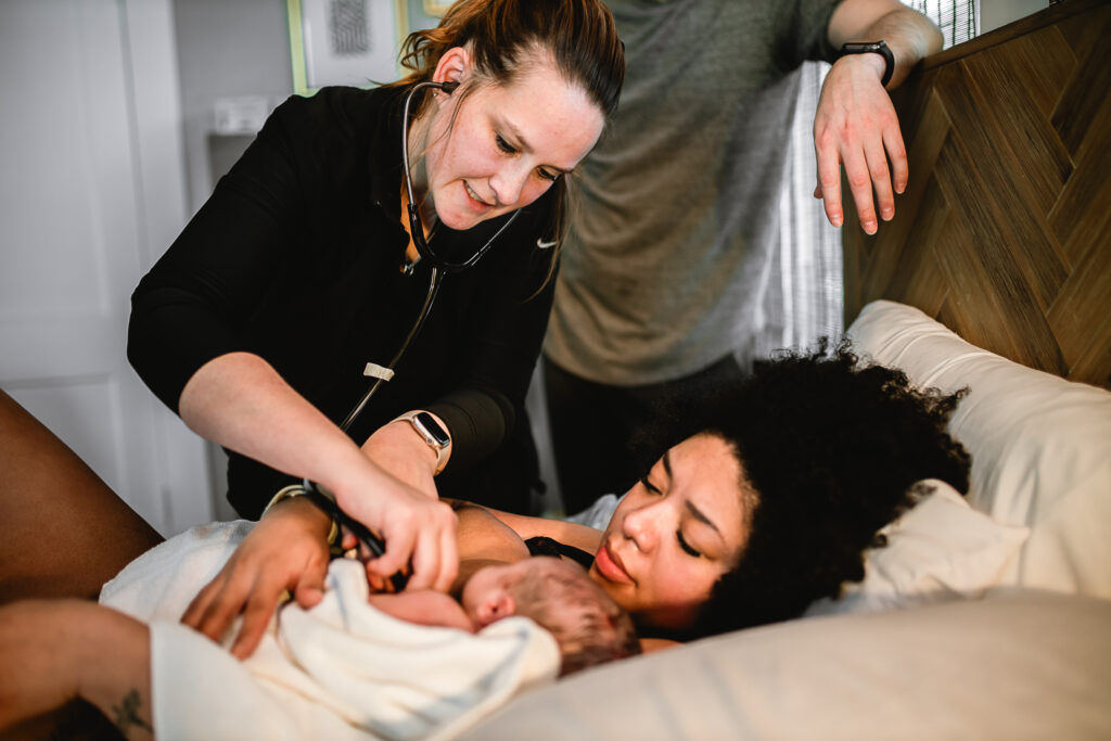 Midwife adjusting the baby’s blanket while the mother lies in bed recovering after birth