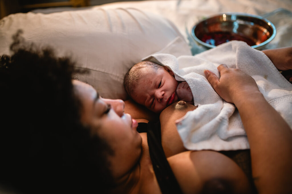 Mother resting in bed at the birth center, holding her newborn on her chest while the placenta rests in a bowl nearby