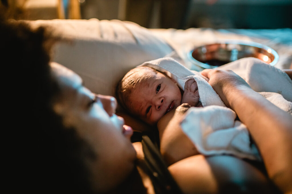 Newborn baby swaddled in a blanket, lying on mother’s chest in the warm golden light of the birth center