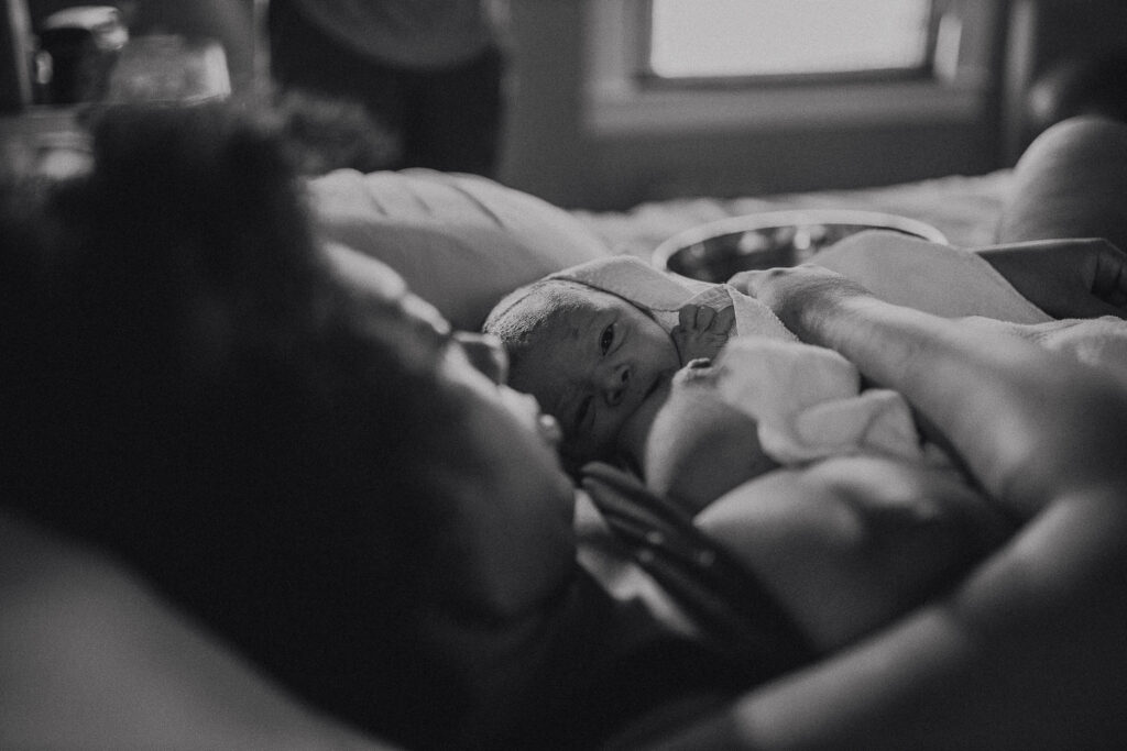 Black and white photo of mother cradling her newborn while resting in bed after birth