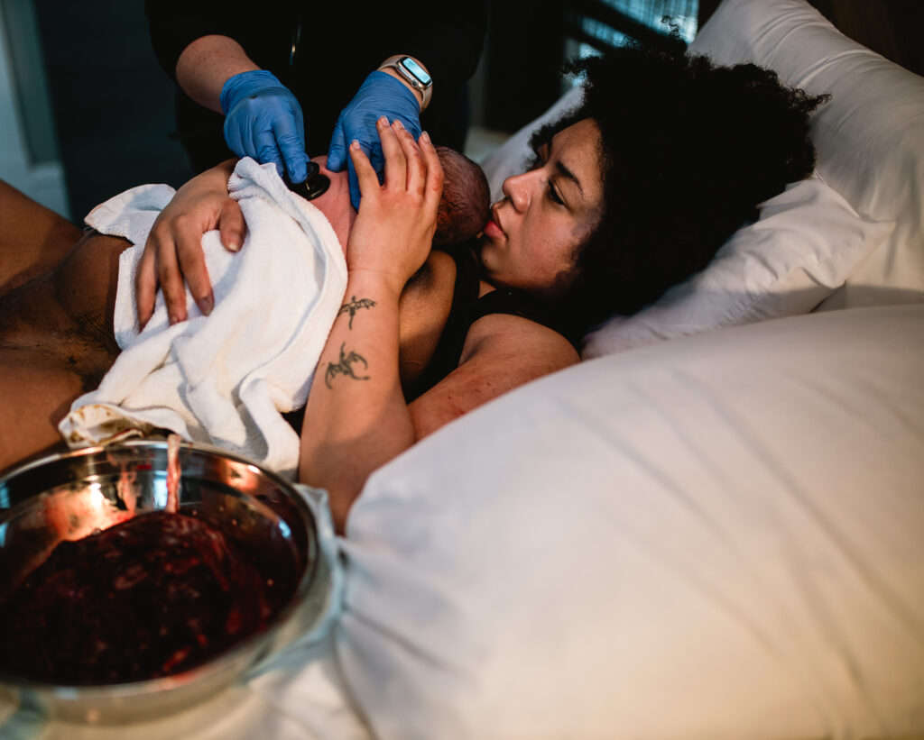 Mother holding her newborn while the birth team assists her during the immediate postpartum period