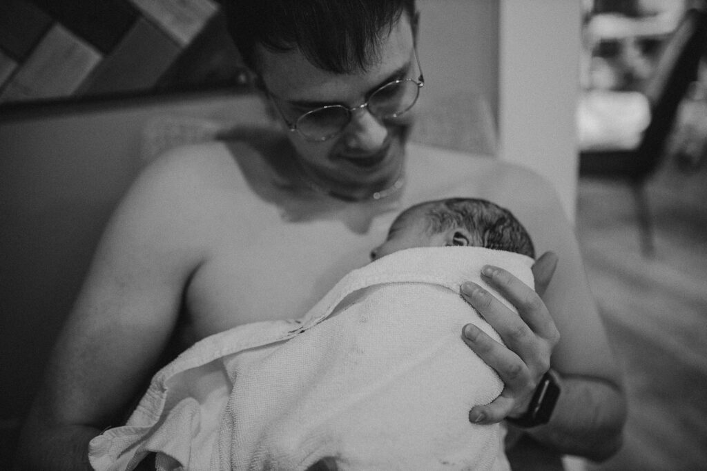 Black and white photo of father gazing down at his newborn wrapped in a blanket
