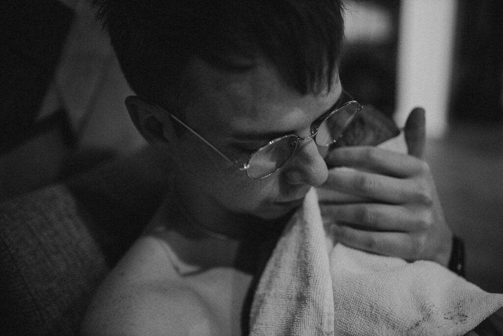 Father wiping tears while cuddling his newborn during an emotional first bonding moment