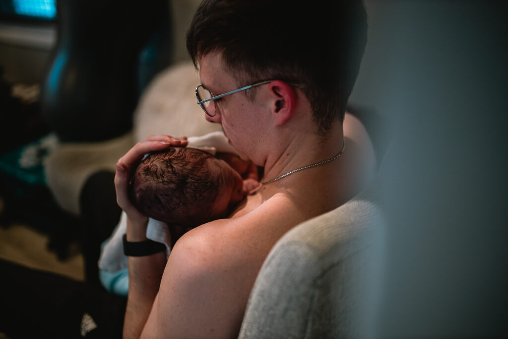 Father sitting and rocking his newborn in his arms under soft evening light at the birth center