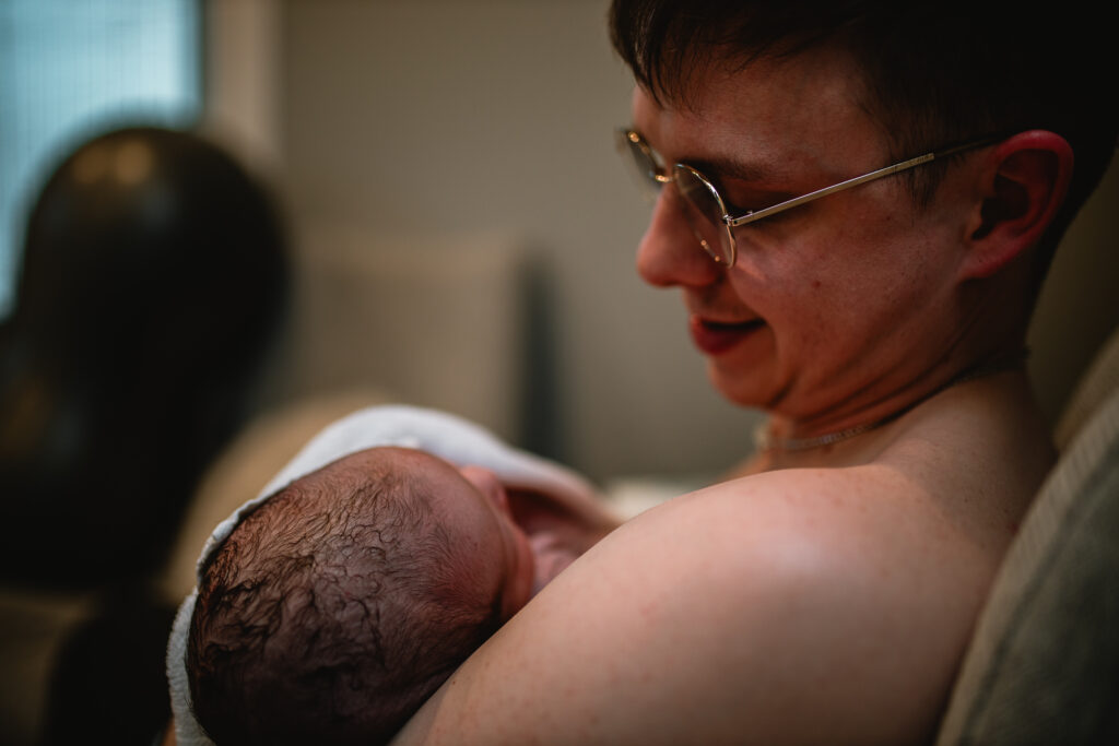 Father proudly holding his newborn baby upright, supporting the baby’s back and shoulders