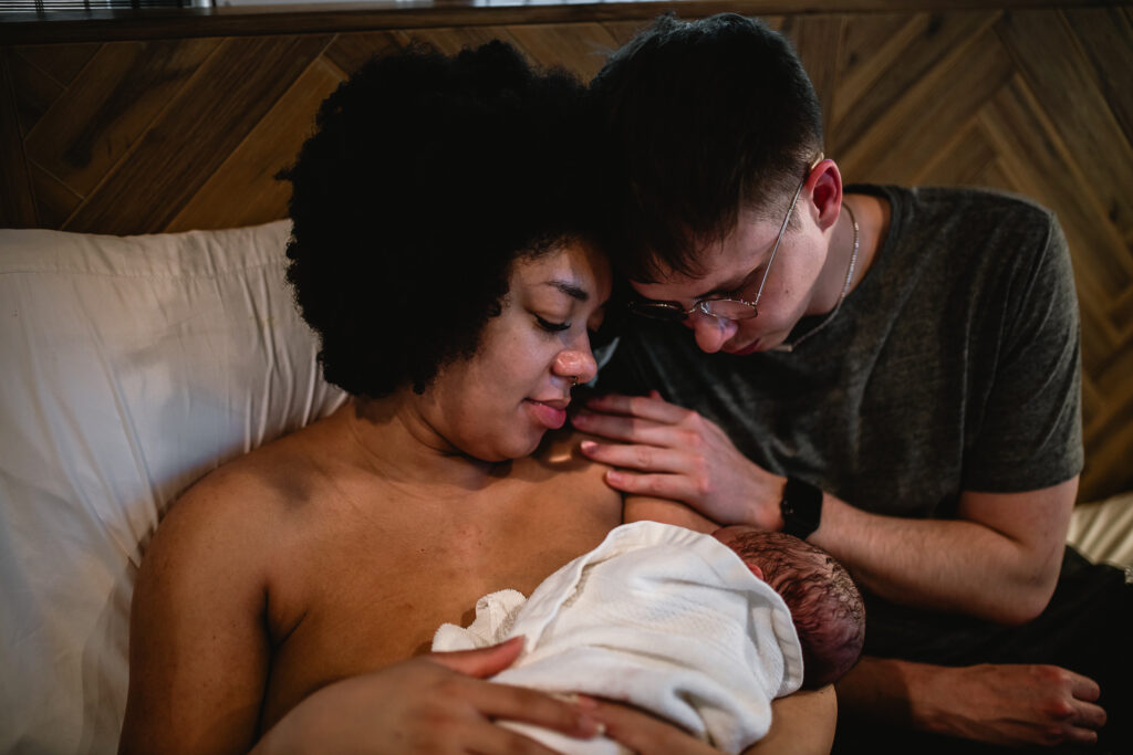 Mother and father cuddling their newborn together in bed, soaking in the first quiet moments as a new family
