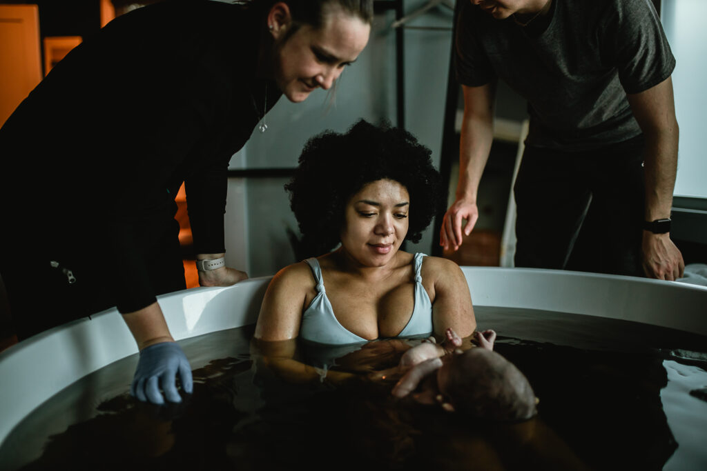 Parents and midwife gently holding baby during herbal bath at the birth center