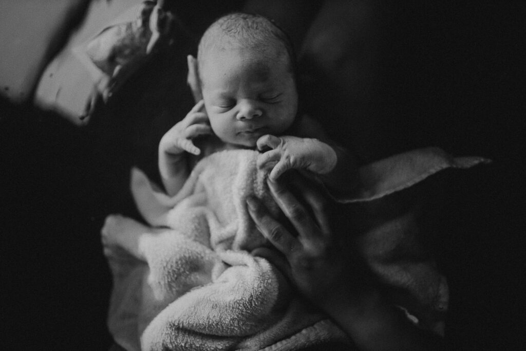 Black and white image of newborn wrapped in towel after herbal bath, peaceful and calm