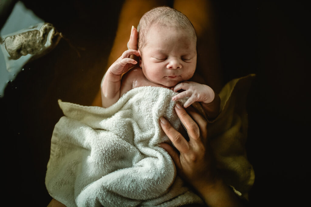 Newborn wrapped in blanket resting in mother’s arms after herbal bath
