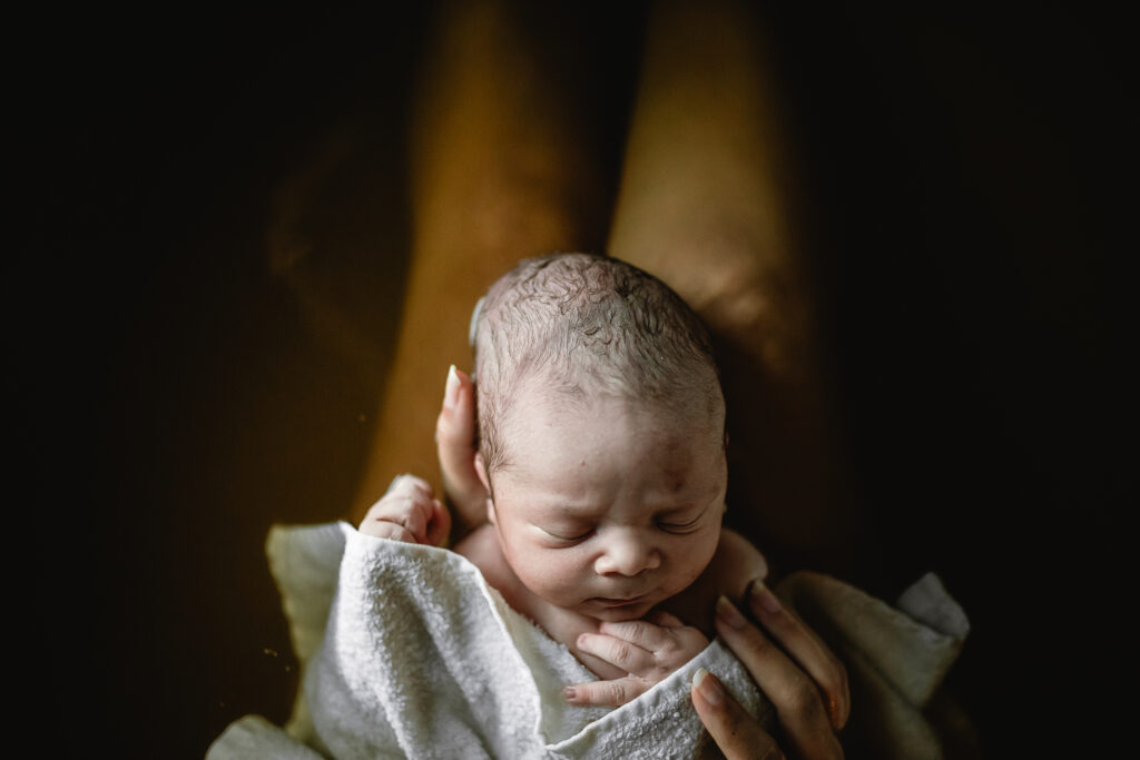Top-down view of newborn’s head resting on mother’s legs during herbal bath
