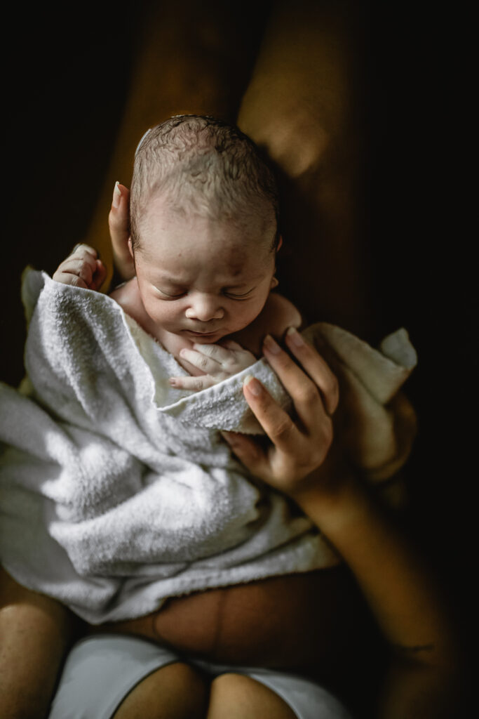 Newborn wrapped in a soft blanket resting in mother’s arms, still fresh from birth