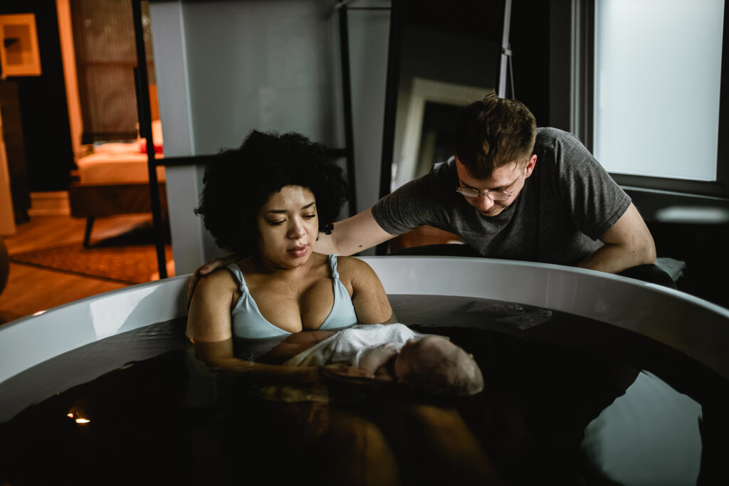 Parents gazing down at their newborn together while sitting in the warm birth tub