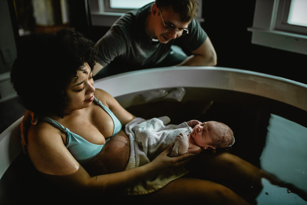 Mother cradling newborn in the herbal bath while father leans close beside her