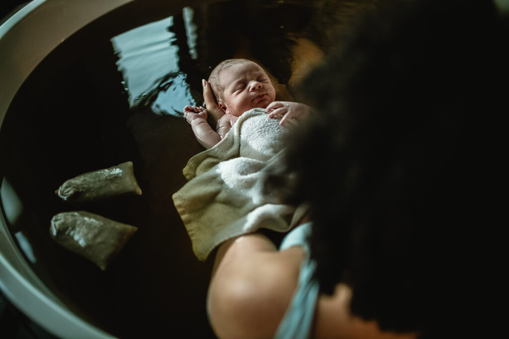 Close-up of newborn resting on mother’s chest in the birth tub during herbal bath