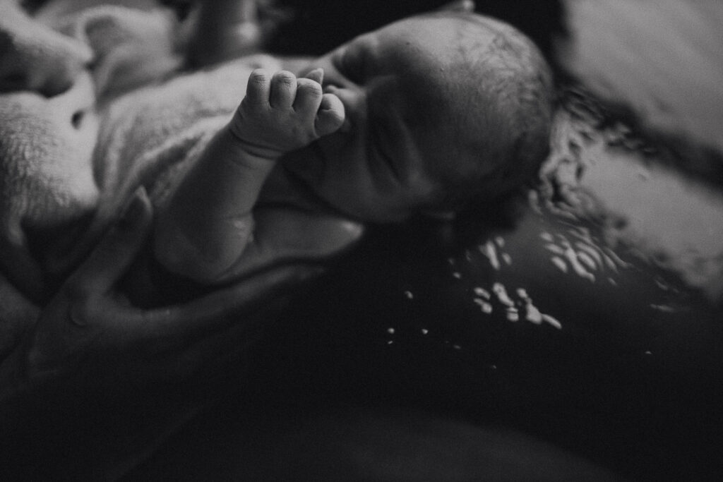 Close-up black and white image of newborn’s face and tiny hand after birth