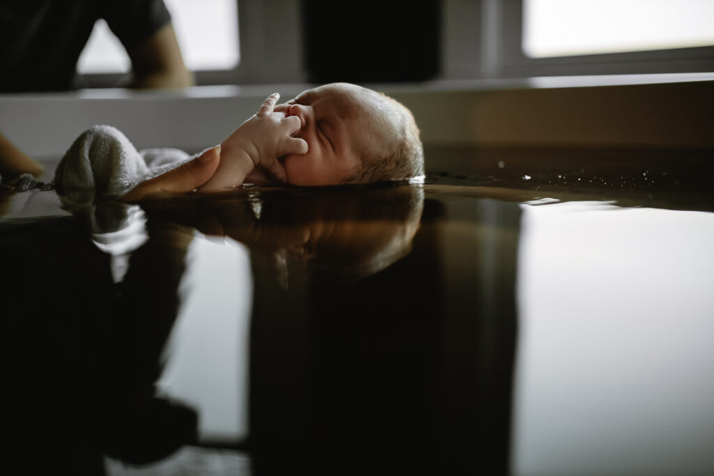 Newborn floating gently in the herbal bath water, eyes closed and calm