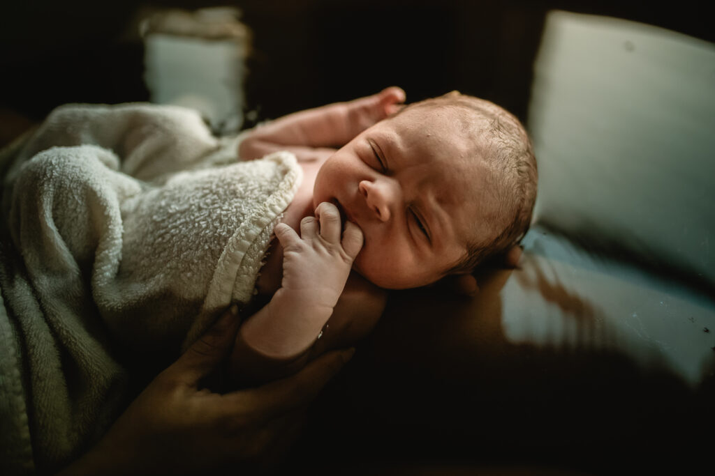 Close-up of newborn’s tiny hand near their face while resting in the herbal bath