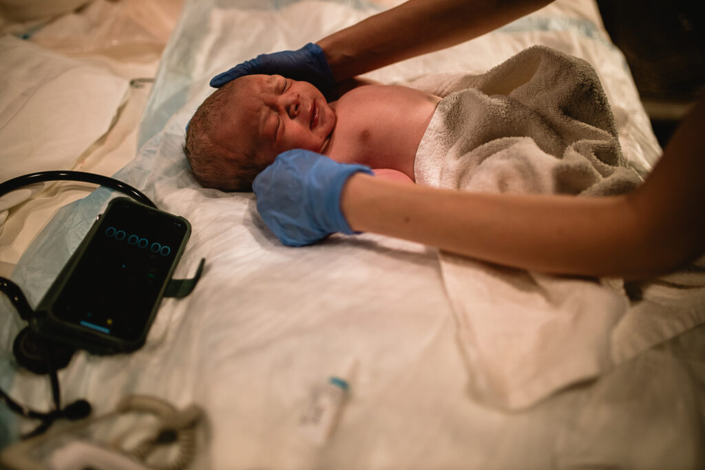 Midwife gently examining newborn on the bed during newborn assessment