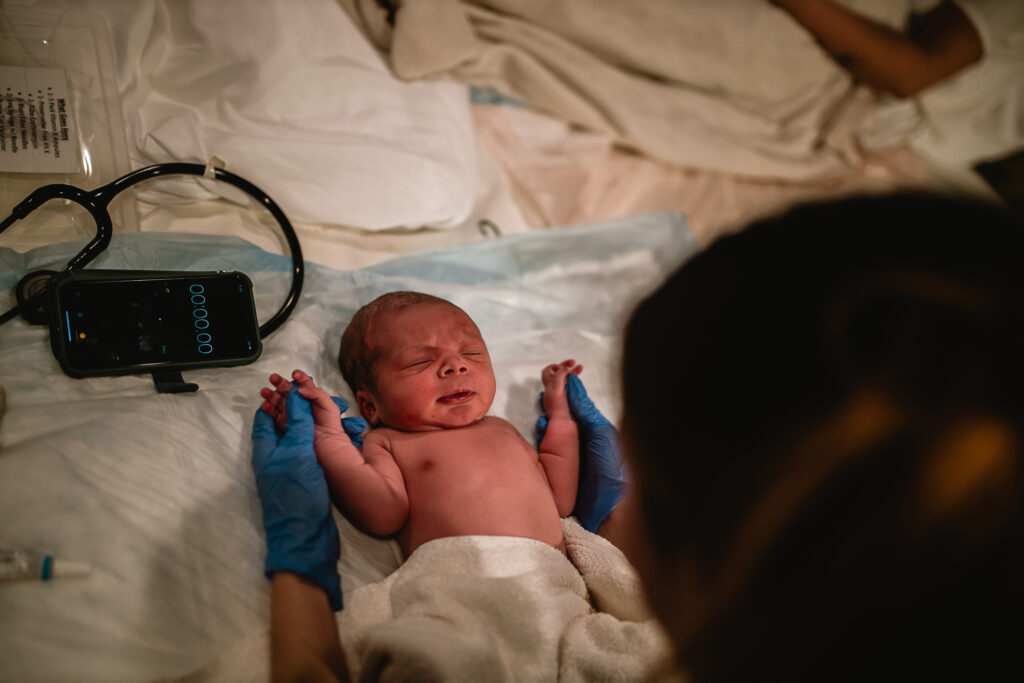 Newborn lying on the bed with gloved hands supporting them during exam