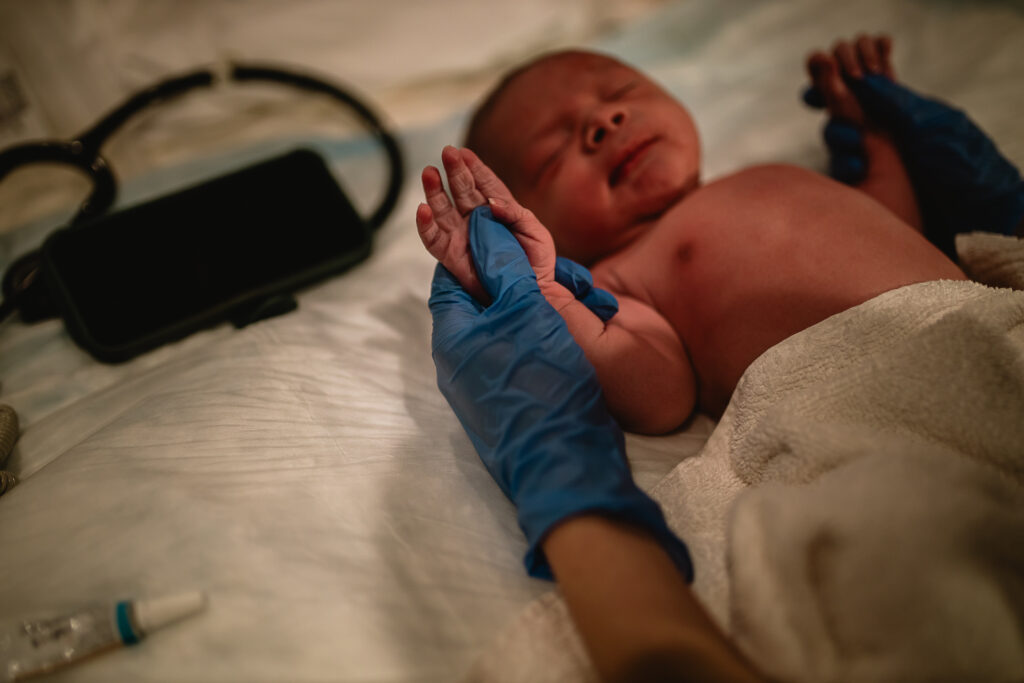 Midwife holding newborn’s tiny hands during routine newborn assessment