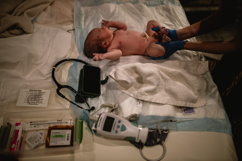Newborn lying on the bed surrounded by medical equipment and exam tools