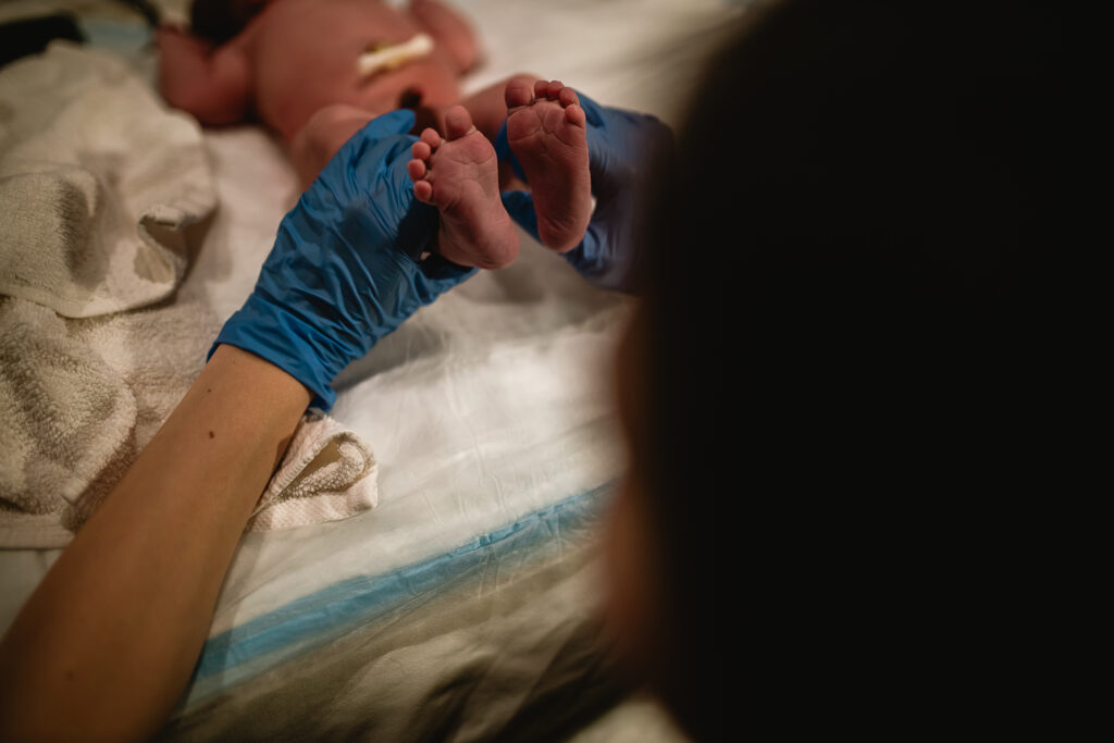 Midwife gently holding newborn’s feet during reflex and tone check