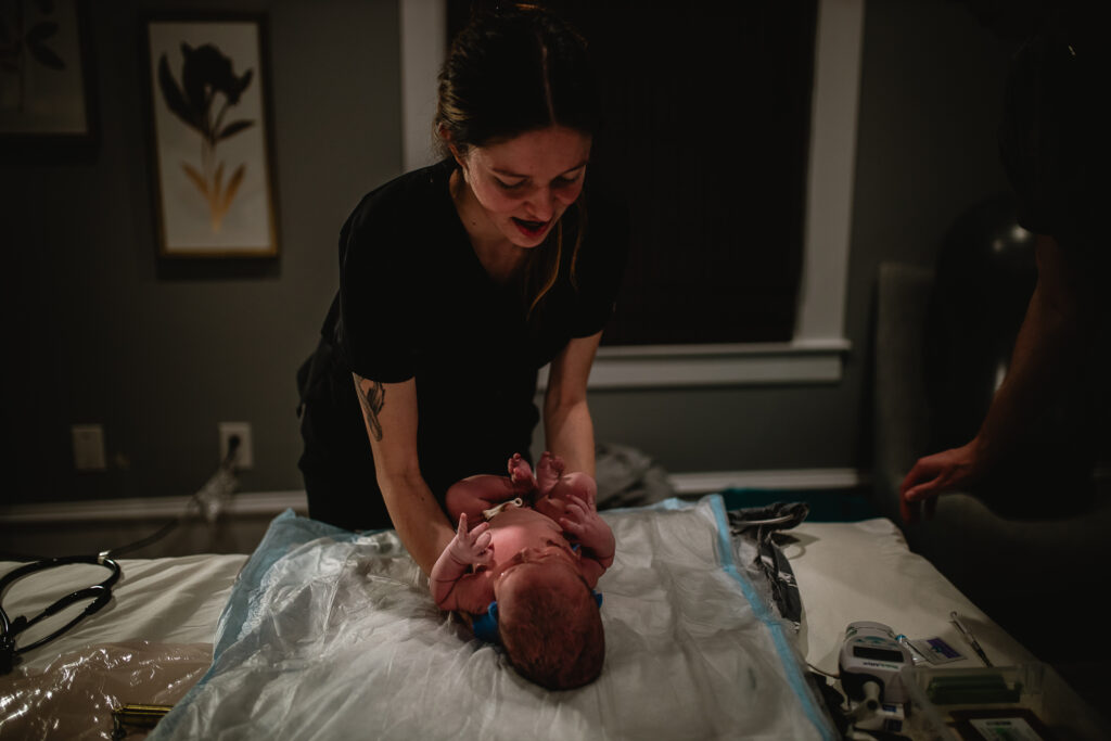 Midwife smiling softly while completing newborn exam on the bed