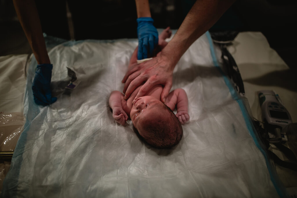 Midwife applying gentle pressure to newborn’s back during check-up