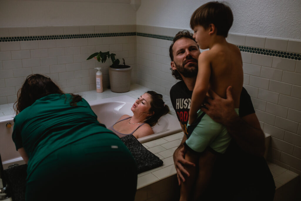 Family-centered home birth — father holding toddler while mother labors in bathroom