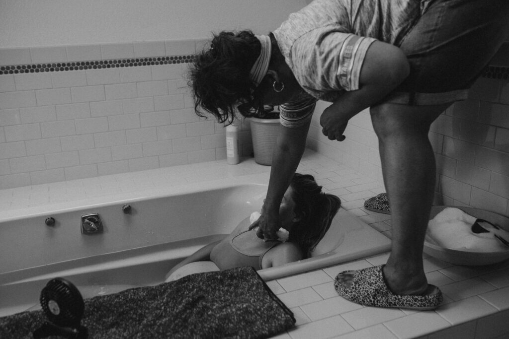 Black and white home birth documentary — mother laboring over bathtub with partner support