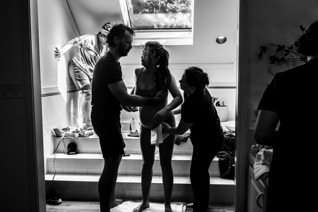 Black and white home birth moment — birth team supporting mother in bathroom before baby’s arrival