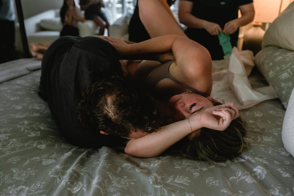 Mother leaning into partner and laboring through transition on bedroom bed during home birth