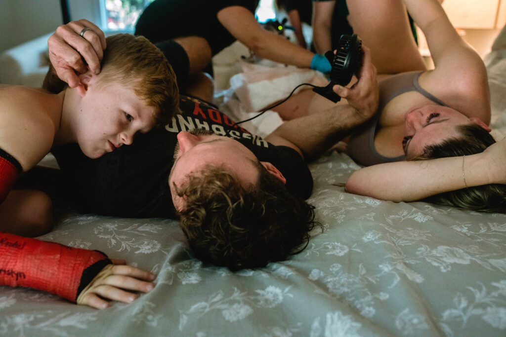 Big brothers cuddling next to their mom after welcoming their new baby sister